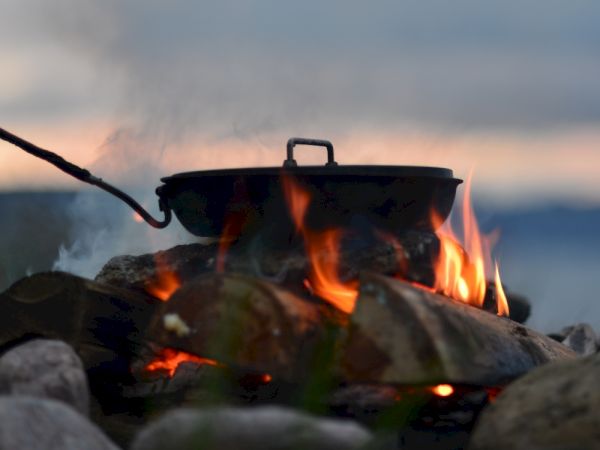 A pot is cooking over an open flame, surrounded by rocks with a scenic background.