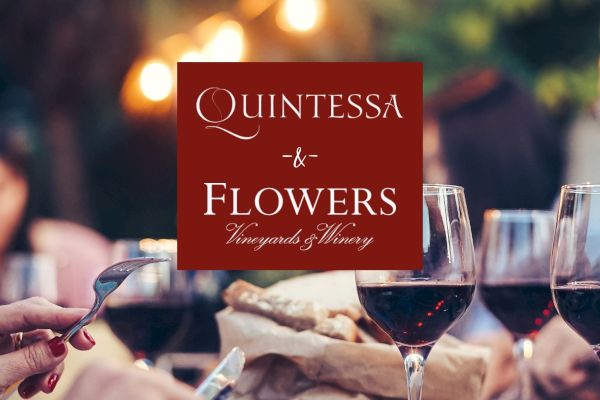 The image shows people dining with red wine, knives, and forks, featuring a "Quintessa & Flowers Vineyards & Winery" sign.