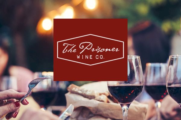 A logo for "The Prisoner Wine Co." overlays an image of people dining with wine glasses and food in a warm, outdoor setting.