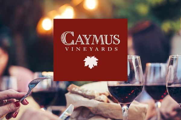 A group of people enjoying wine outdoors, with a Caymus Vineyards logo overlaying the image.