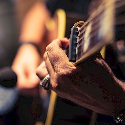 A close-up of a person playing an acoustic guitar, focusing on the hand and strings, with a blurred background.