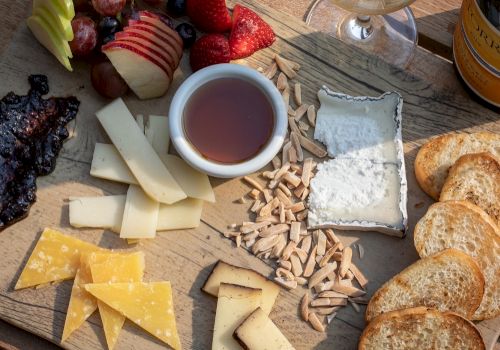 A charcuterie board with assorted cheeses, fruits, nuts, bread slices, and a dip, accompanied by a glass of white wine on the side.