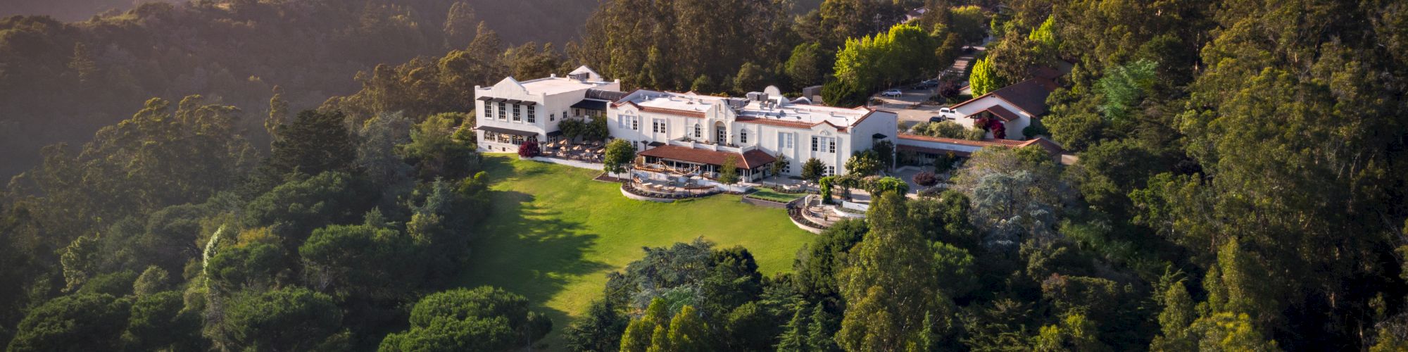 A large estate surrounded by lush greenery and rolling hills under a clear blue sky.