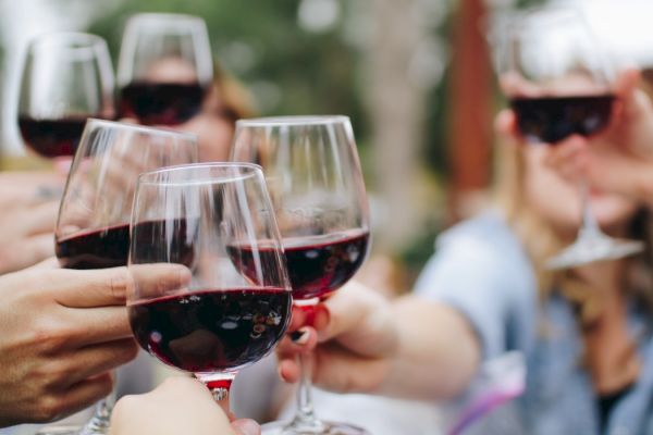 People clinking glasses of red wine in a celebratory toast, blurred background.