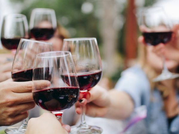 People clinking glasses of red wine in a celebratory toast, blurred background.