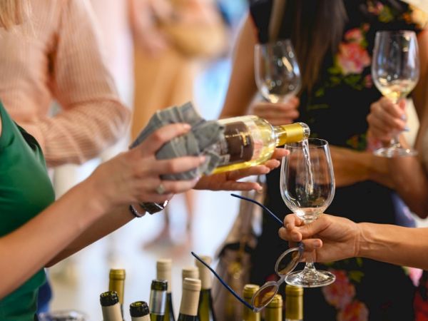 People at a social gathering are pouring white wine into glasses. Bottles are in the foreground.