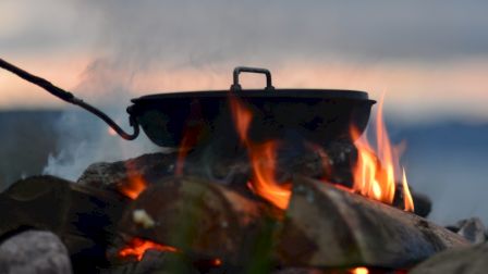 A pot is cooking over an open flame, surrounded by rocks with a scenic background.