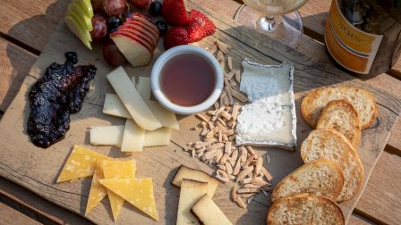 A charcuterie board with cheeses, sliced apples, strawberries, grapes, jam, honey, nuts, crackers, and a bottle of wine on the side.