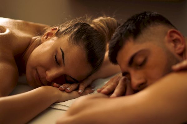 Two people are lying face down on massage tables, appearing relaxed.
