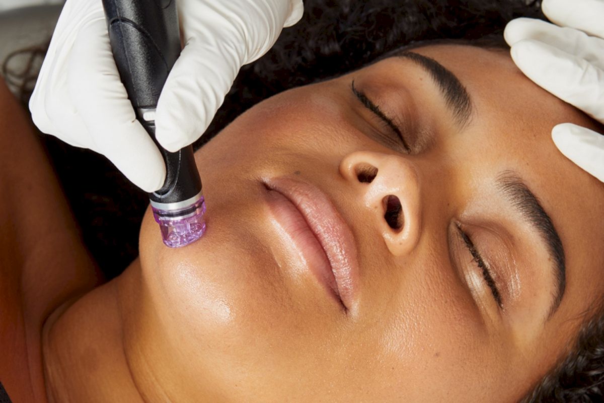 A person receives a facial treatment using a handheld device, wearing white gloves, with eyes closed.