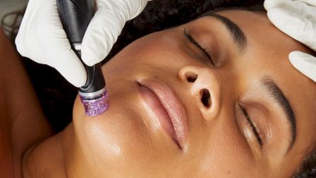 A person receiving a facial treatment with a handheld device, applied by someone wearing gloves.