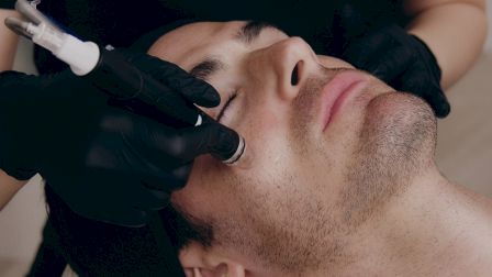 A person is receiving a facial treatment with a device, while a technician wearing black gloves performs the procedure.