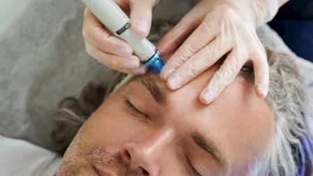 A person is receiving a facial treatment with a device, handled by someone wearing gloves, while lying down and relaxing.