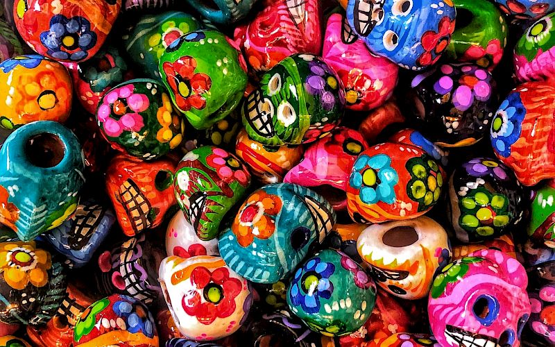 Colorful Day of the Dead skull decorations with various designs, featuring flowers and vibrant patterns, are tightly packed together.