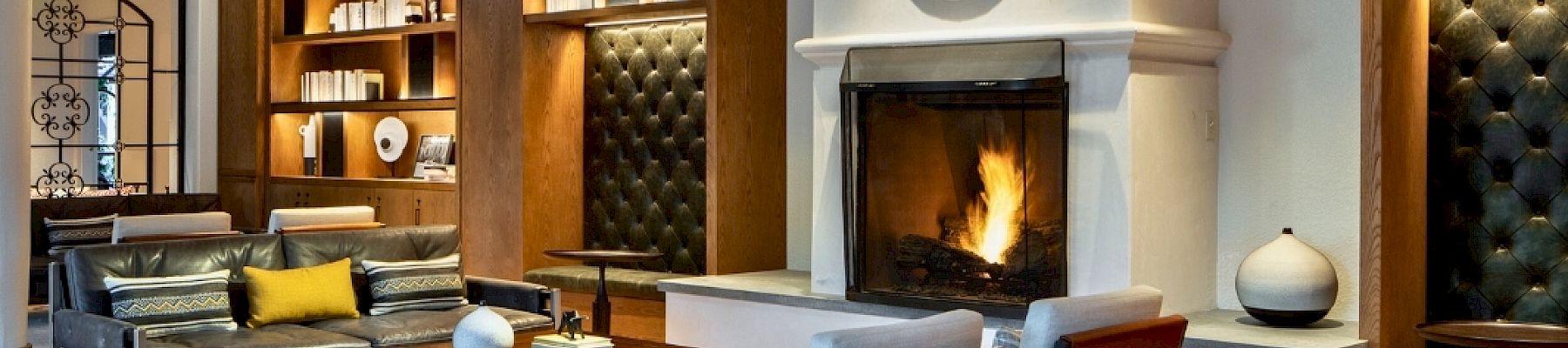 A cozy, modern living room with a fireplace, built-in shelves, and mid-century seating arranged around a rug and warm lighting.