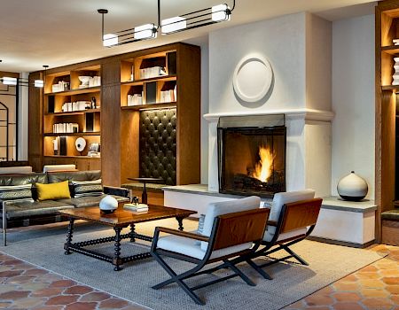 A cozy, modern living room with a fireplace, built-in shelves, and mid-century seating arranged around a rug and warm lighting.
