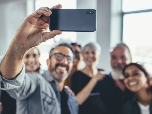 A group of smiling people taking a selfie with a smartphone, crowding in close and posing for the photo.